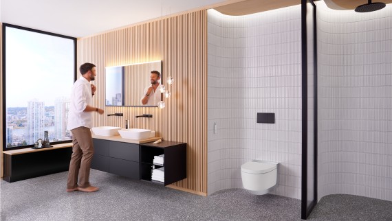 Man in bathroom standing in front of Geberit Option Plus Square mirror and black Geberit ONE bathroom furniture (© Geberit) Man in bathroom standing in front of Geberit Option Plus Square mirror and black Geberit ONE bathroom furniture (© Geberit)